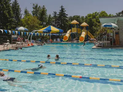Outdoor swimming pool with lap lanes, zipline, slides. and shaded seating.