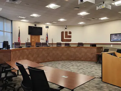 City Council chamber showing a rounded desk, chairs, and Louisville logo.