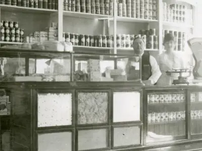 A black and white photo of a man and a woman standing behind a shop counter.