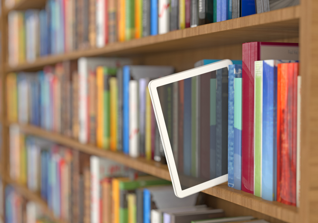 A tablet ereader is positioned on a shelf, with a bookcase filled with various books in the background.