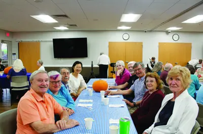 Older adults gather around a table with a pumpkin at a senior center event.