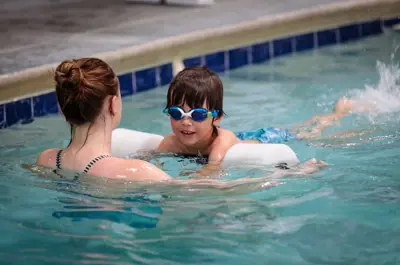 Adult helping a child practice swimming in an indoor pool.