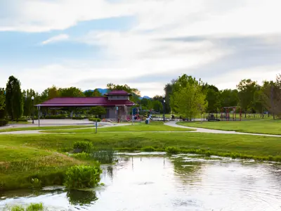 A pond and grassy field with a park shelter in the background.