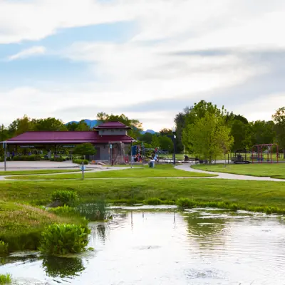 A pond and grassy field with a park shelter in the background.