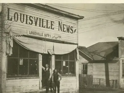 A black and white photo of a small building with awning and a sign reading Louisville News.