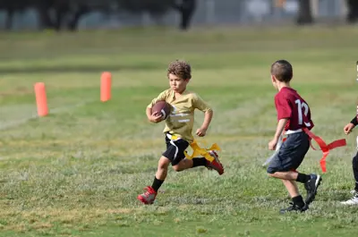 Two children playing flag football on a grassy field.