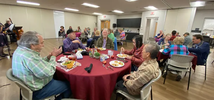 Older adults share a meal at round tables during a Brooks Cafe Lunch.