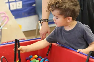 Young child plays with colorful balls in a sensory bin.