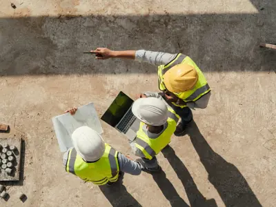 Overhead shot of three people in hard hats and safety gear at a construction site.
