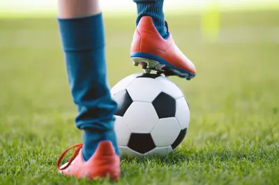 Soccer player standing with one foot on a ball.