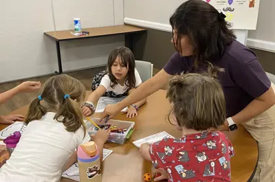 Adult guides children through a coloring activity at a table.