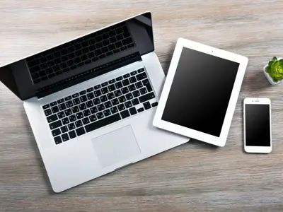 laptop, smartphone, and tablet, with small green plant on wooden table