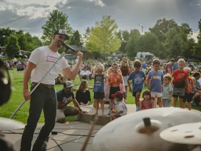A man singing into a microphone in front of a group of children outside.